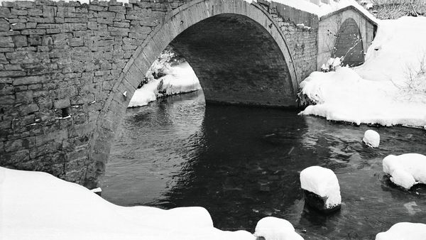 Ura e vjetër me hark guri mbi lumin Klina, me brigjet të mbuluara me dëborë