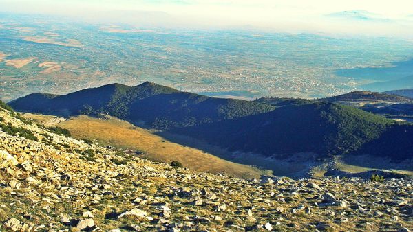 Pamje nga lart e Pejës dhe e Rrafshit të Dukagjinit, me kodra të pyllëzuara e gurë në plan të parë