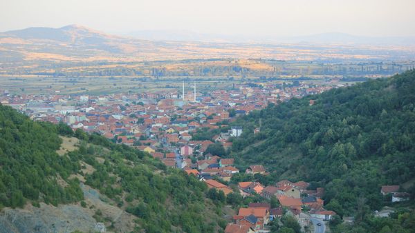 Qyteti i Preshevës me çatitë e kuqe dhe dy minare, parë nga kodrat me pyll mbi të, me fushën e luginës pas