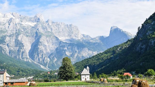 Kisha e vogël e Thethit me kambanore dhe çati me dërrasa, mes livadhesh me kapica bari, nën muret shkëmbore të Alpeve