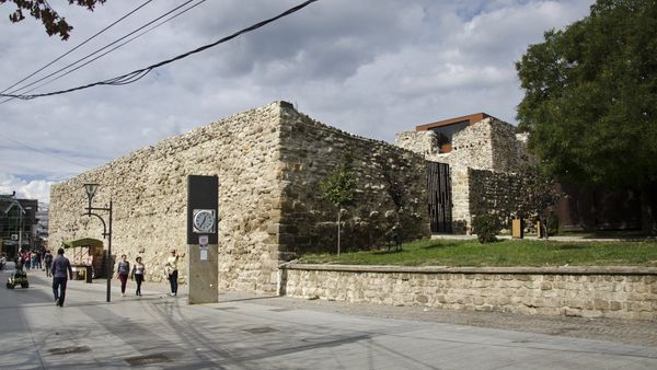 Muret prej guri të kalasë së Vushtrrisë dhe kulla e saj në qendër të qytetit, me një shesh të shtruar ku ecin kalimtarë