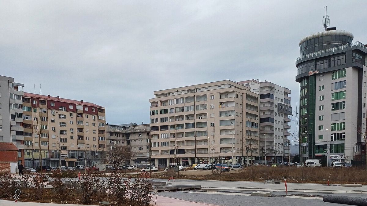 Një shesh i ri i shtruar me kubëza në Drenas, me pallate banimi dhe një ndërtesë të lartë me kupolë xhami në sfond, në një ditë me re