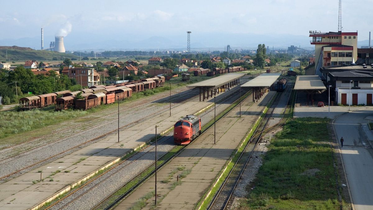 Stacioni hekurudhor i Fushë Kosovës parë nga lart, me peronë të mbuluar, një lokomotivë të kuqe, vagonë mallrash dhe rrafshin me termocentralin e Obiliqit në sfond