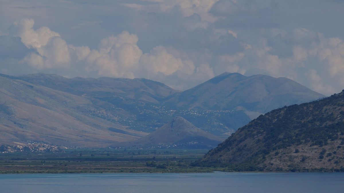 Pamje nga Korfuzi përtej ngushticës: fusha e Vrinës me kodrën e Çukës së Ajtoit dhe, në shpatet e maleve në sfond, shtëpitë e Konispolit