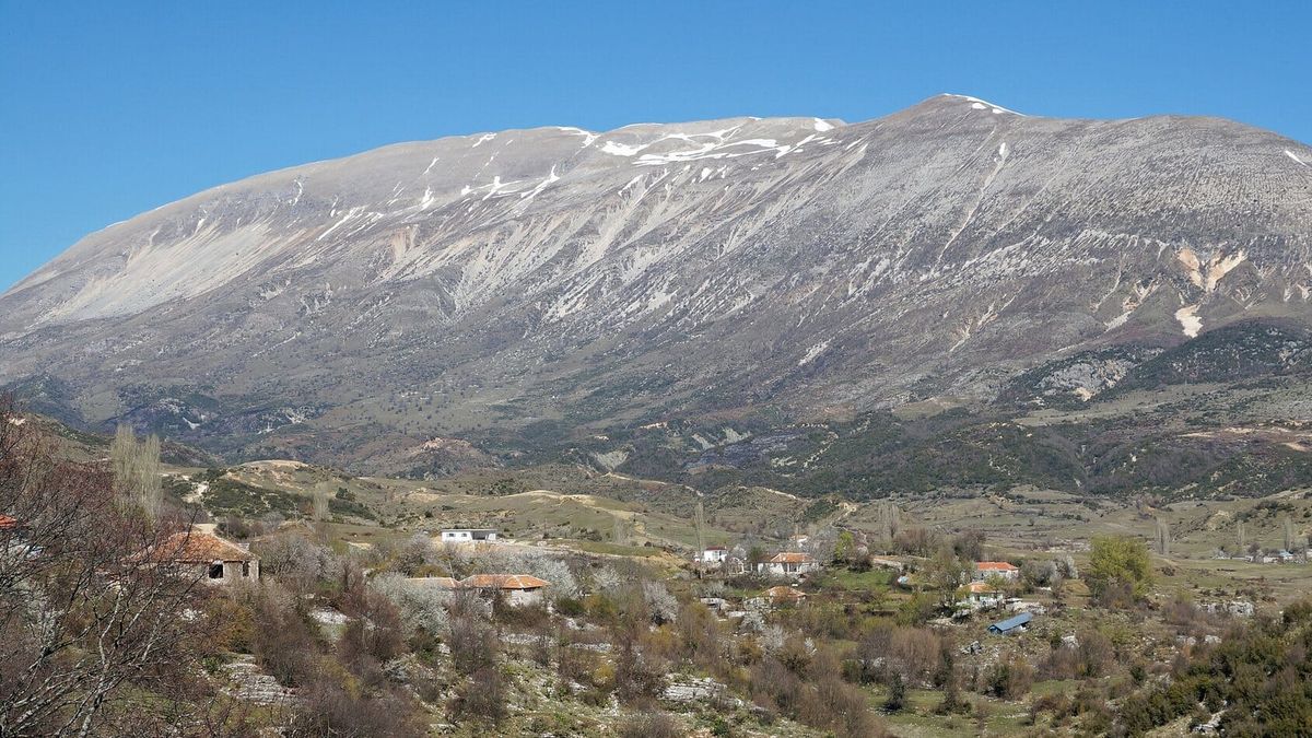Mal i lartë gëlqeror me pak dëborë, parë nga fshati Nivicë i Kurveleshit, me shtëpitë e fshatit në plan të parë