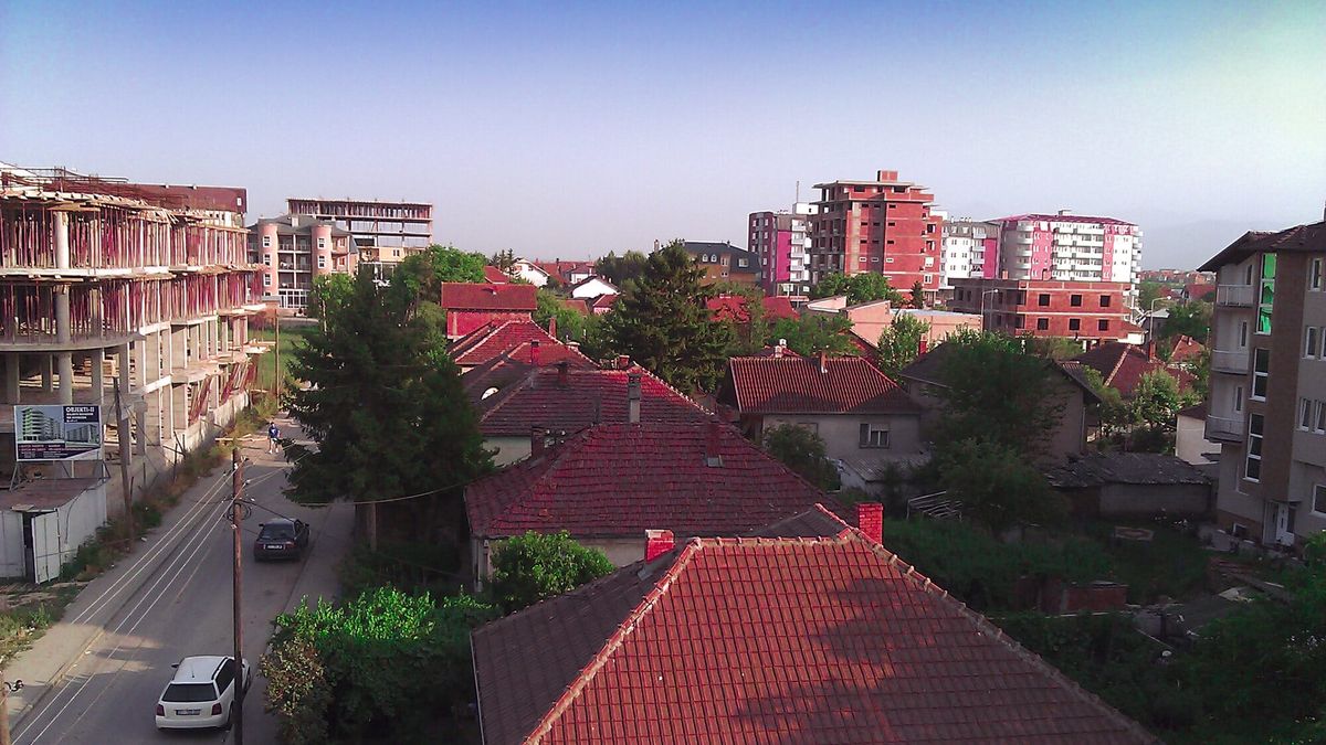 Pamje e Lipjanit nga lart: shtëpi me çati të kuqe në plan të parë, pallate shumëkatëshe në sfond dhe një rrugë me makina në të majtë