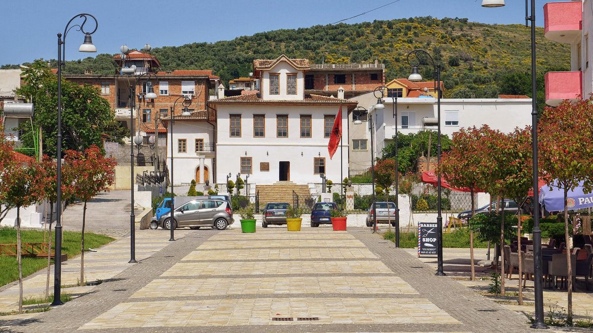 Shtëpia dykatëshe e bardhë e Muzeut të Kongresit të Lushnjës, me flamurin kombëtar para saj dhe kodrat me ullinj prapa