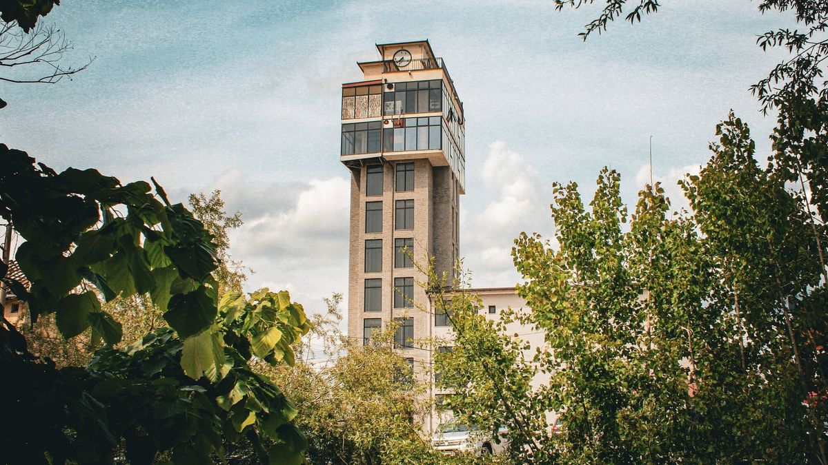 Sahatkulla e Malishevës, ndërtesë e lartë me orë në majë, e parë mes pemëve të gjelbra