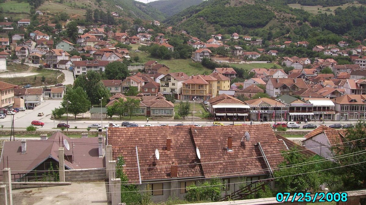 Qyteti i Kaçanikut me shtëpi me çati të kuqe dhe kodra të pyllëzuara pas tyre