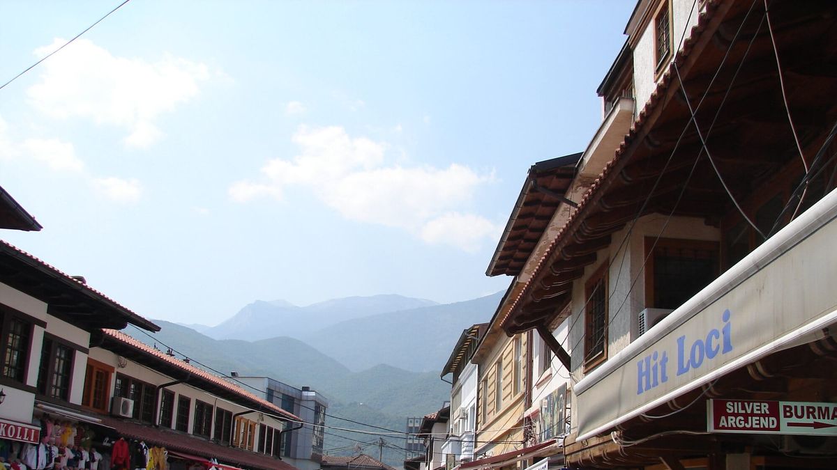 Rruga e Çarshisë së Gjatë të Pejës me dyqane e kalimtarë, me malet në sfond