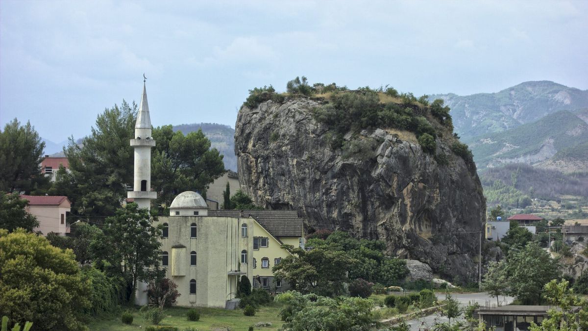 Guri i Qytetit në Përmet, shkëmb i madh gëlqeror i mbuluar me shkurre, me një xhami me minare në plan të parë dhe malet e luginës së Vjosës pas