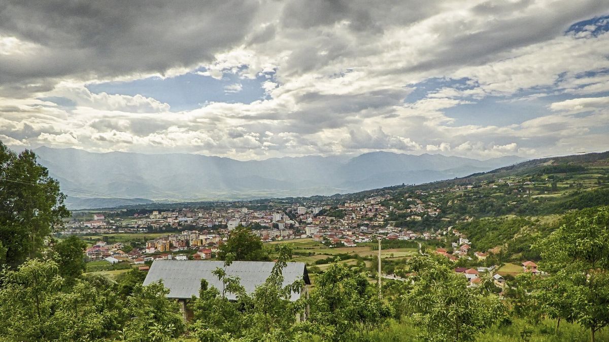 Pamje e Peshkopisë nga kodrat në jugperëndim të qytetit, me shtëpitë në luginë dhe malet e Dibrës në sfond nën qiell me re