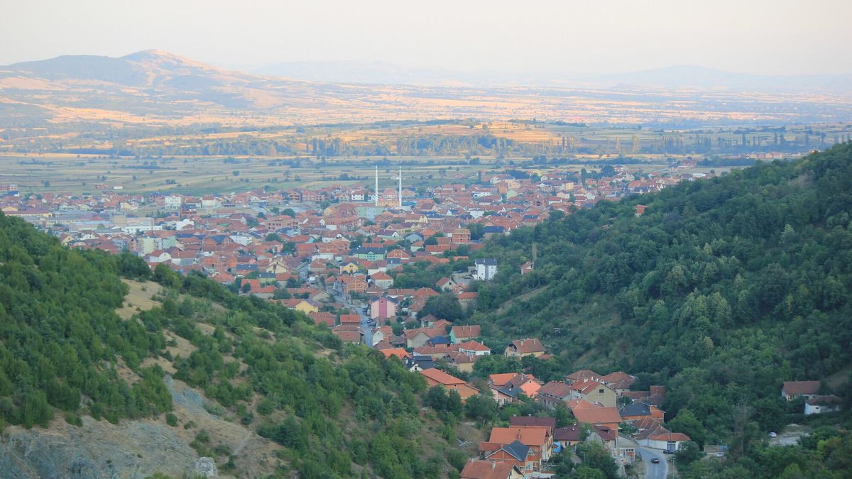 Qyteti i Preshevës me çatitë e kuqe dhe dy minare, parë nga kodrat me pyll mbi të, me fushën e luginës pas